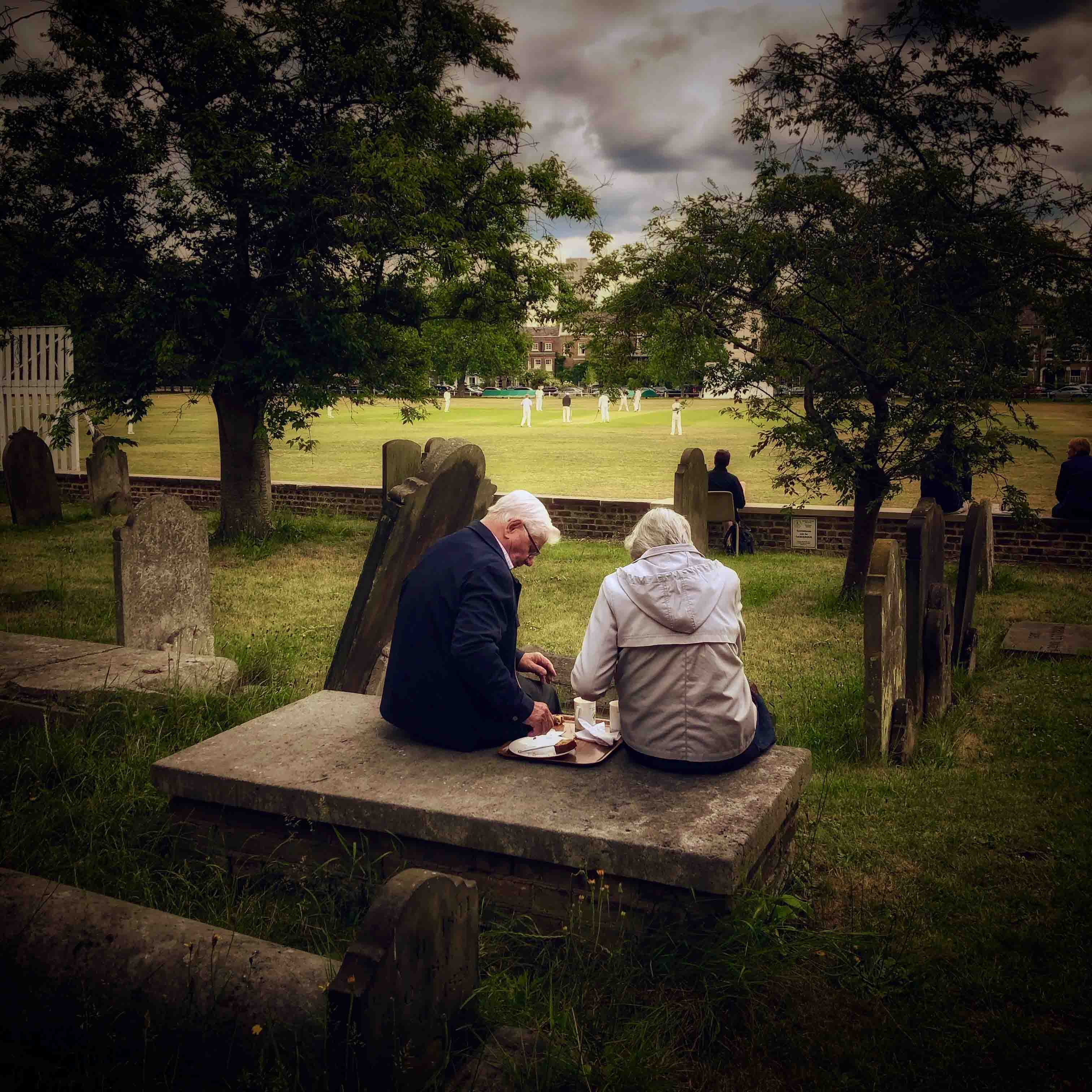 A couple enjoy afternoon tea in the graveyard of St Anne’s church while watching cricket on Kew Green, close to the Royal Botanic Gardens.